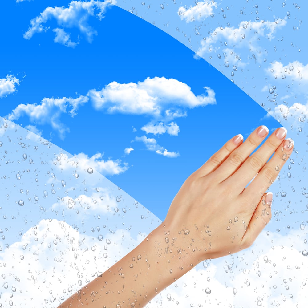 Hand wipes misted window at a blue sky