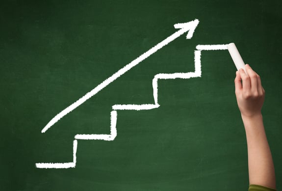 Stairs heading upwards with an arrow drawn by hand on a green chalkboard.